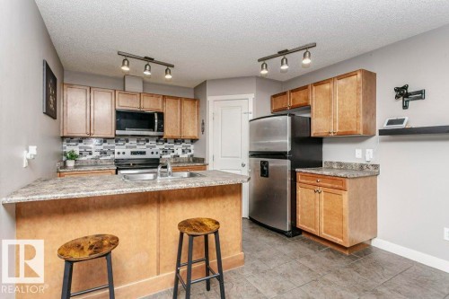 Kitchen with a kitchen bar, stainless steel appliances, rail lighting, decorative backsplash, and a peninsula - 1381 Rutherford Road, Edmonton, AB - Indoor Photo Showing Kitchen With Stainless Steel Kitchen With Double Sink