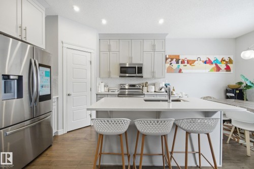Kitchen featuring stainless steel appliances, a kitchen bar, dark wood-style floors, an island with sink, and tasteful backsplash - 9942 222A St Nw, Edmonton, AB - Indoor Photo Showing Kitchen With Upgraded Kitchen