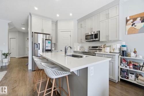 Kitchen with dark wood-style flooring, a breakfast bar, light stone counters, stainless steel appliances, and recessed lighting - 9942 222A St Nw, Edmonton, AB - Indoor Photo Showing Kitchen With Upgraded Kitchen