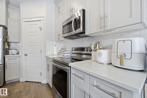 Kitchen featuring stainless steel appliances, light wood-style floors, white cabinetry, and light stone countertops - 9942 222A St Nw, Edmonton, AB - Indoor Photo Showing Kitchen