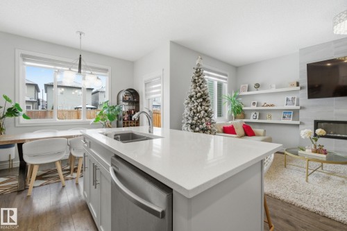 Kitchen featuring stainless steel dishwasher, a chandelier, light stone counters, a fireplace, and dark wood-style floors - 9942 222A St Nw, Edmonton, AB - Indoor Photo Showing Other Room With Fireplace