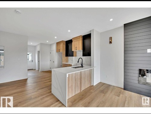Kitchen featuring light wood-style flooring, light stone countertops, a fireplace, a peninsula, and recessed lighting - 426 Crystal Creek Link, Leduc, AB - Indoor Photo Showing Other Room