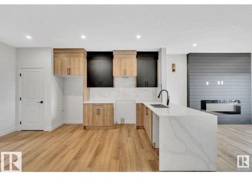 Kitchen featuring light stone counters, a peninsula, light wood finished floors, modern cabinets, and recessed lighting - 426 Crystal Creek Link, Leduc, AB - Indoor Photo Showing Kitchen With Double Sink