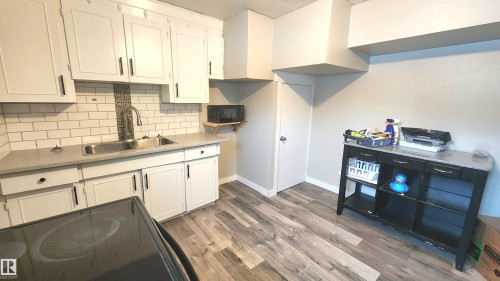 Kitchen featuring black appliances, backsplash, light wood-style flooring, and white cabinets - 12139 81 Street, Edmonton, AB - Indoor Photo Showing Kitchen With Double Sink