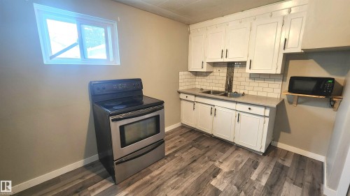 Kitchen featuring electric range, white cabinets, decorative backsplash, and light countertops - 12139 81 Street, Edmonton, AB - Indoor Photo Showing Kitchen With Double Sink