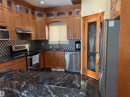 Kitchen featuring stainless steel appliances, wood finish cabinets, granite floors, glass insert cabinets, and backsplash - 816 Wildwood Crescent Nw, Edmonton, AB - Indoor Photo Showing Kitchen With Stainless Steel Kitchen