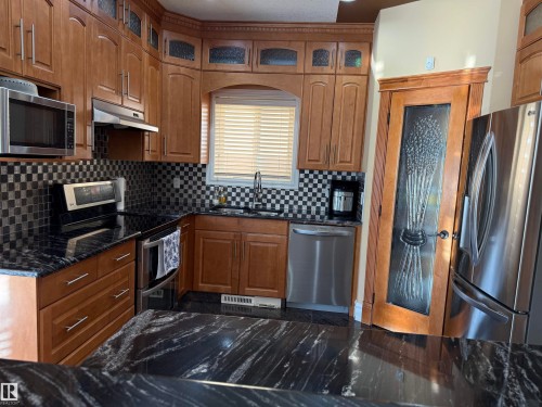 Kitchen with stainless steel appliances, glass insert cabinets, wood finish cabinets, backsplash, and dark stone counters - 816 Wildwood Crescent Nw, Edmonton, AB - Indoor Photo Showing Kitchen With Stainless Steel Kitchen