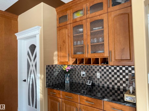 Kitchen featuring glass fronted cabinets, wood finish cabinets, tasteful backsplash, and dark stone counters - 816 Wildwood Crescent Nw, Edmonton, AB - Indoor