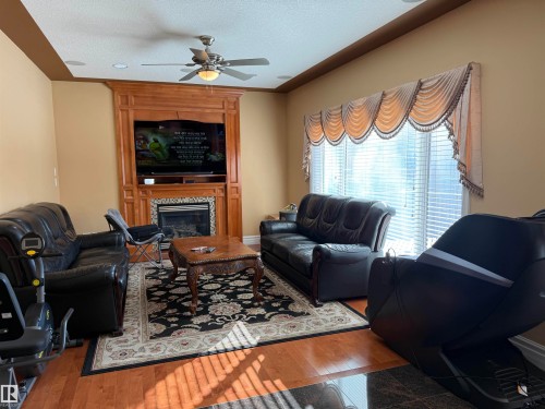 Living area with a ceiling fan, a tiled fireplace, wood finished floors, and a textured ceiling - 816 Wildwood Crescent Nw, Edmonton, AB - Indoor Photo Showing Living Room With Fireplace