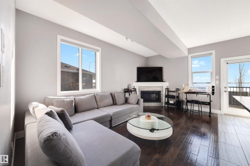 Living room featuring a glass covered fireplace and dark wood-style flooring - 81 Richmond Link, Fort Saskatchewan, AB - Indoor Photo Showing Living Room With Fireplace