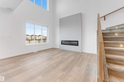 Unfurnished living room with a fireplace, light wood-style flooring, stairs, healthy amount of natural light, and a towering ceiling - 
