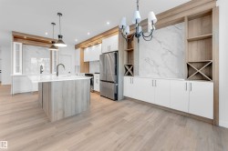 Kitchen with decorative light fixtures, appliances with stainless steel finishes, white cabinets, modern cabinets, and light brown cabinetry - 