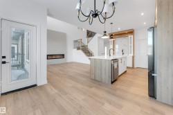 Kitchen with an island with sink, a glass covered fireplace, open floor plan, light stone counters, and hanging light fixtures - 
