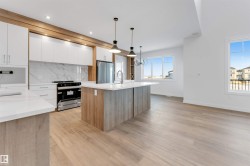 Kitchen featuring white cabinets, appliances with stainless steel finishes, modern cabinets, light stone countertops, and decorative light fixtures - 