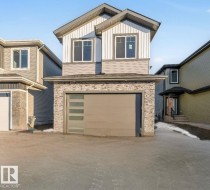 View of front of property with board and batten siding, driveway, an attached garage, and stone siding - 