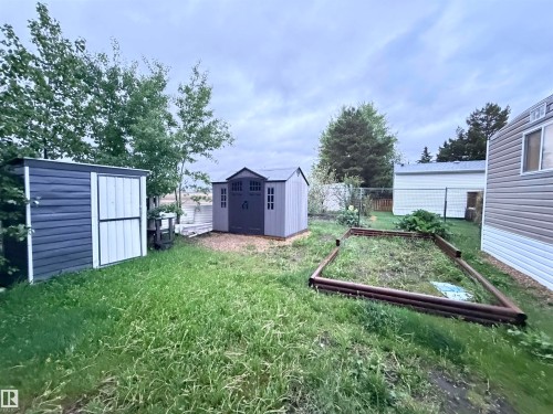 Backyard featuring two storage sheds, a raised garden bed, and mature trees - 68 9501 104 Avenue, Westlock, AB 
