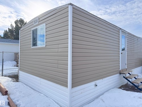 Manufactured home exterior featuring tan horizontal siding, white trim, a white entry door with glass paneling, a white framed window, and a white foundation skirting - 68 9501 104 Avenue, Westlock, AB 