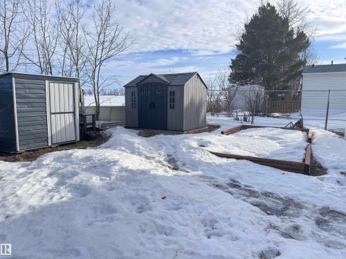 Two outdoor storage sheds, one featuring a vertical panel door and the other with double doors, are situated on the property - 68 9501 104 Avenue, Westlock, AB 
