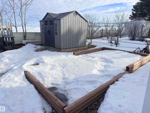 Backyard featuring a grey storage shed with dark double doors, a fenced perimeter, and a raised garden bed with log-style timber borders - 68 9501 104 Avenue, Westlock, AB 