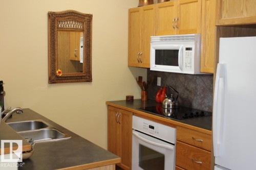 Kitchen with white appliances, dark countertops, and decorative backsplash - 330 4831 104A Street, Edmonton, AB - Indoor Photo Showing Kitchen With Double Sink