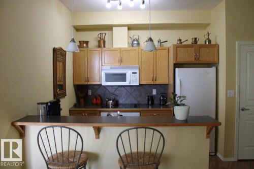 Kitchen with a breakfast bar, white appliances, pendant lighting, dark countertops, and decorative backsplash - 330 4831 104A Street, Edmonton, AB - Indoor Photo Showing Kitchen
