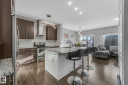 Kitchen featuring light stone countertops, appliances with stainless steel finishes, open floor plan, a kitchen bar, and dark brown cabinets - 
