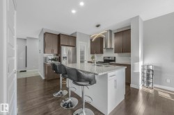 Kitchen featuring light stone countertops, stainless steel appliances, decorative backsplash, dark brown cabinets, and wall chimney exhaust hood - 