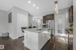 Kitchen featuring stainless steel appliances, light stone countertops, dark brown cabinets, a kitchen island with sink, and dark wood-style flooring - 