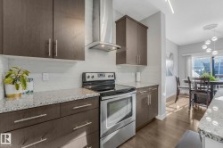 Kitchen with stainless steel electric stove, wall chimney range hood, light stone countertops, and dark brown cabinets - 