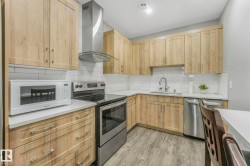 Kitchen with stainless steel appliances, wall chimney exhaust hood, light brown cabinets, tasteful backsplash, and light wood-type flooring - 