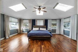 Bedroom featuring a skylight, hardwood / wood-style floors, a ceiling fan, multiple windows, and vaulted ceiling - 