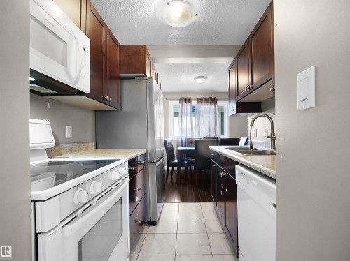 Kitchen featuring white appliances, light countertops, a textured ceiling, dark brown cabinetry, and light tile patterned flooring - 791 Abbottsfield Road, Edmonton, AB - Indoor Photo Showing Kitchen With Upgraded Kitchen