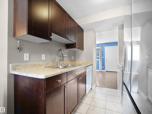 Kitchen with dark brown cabinetry, a textured ceiling, white dishwasher, stainless steel range oven, and light tile patterned floors - 791 Abbottsfield Road, Edmonton, AB - Indoor Photo Showing Kitchen With Double Sink