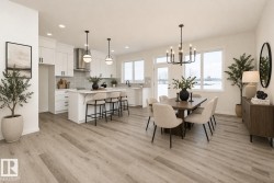 This open-concept living area features light-colored flooring, a modern kitchen with white cabinetry and a center island, and a dining area with a chandelier - 