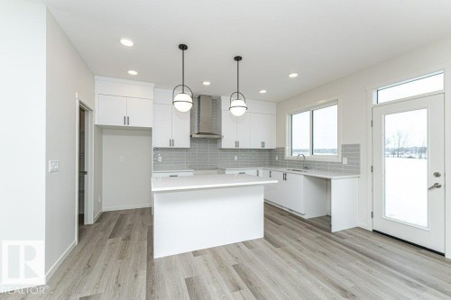 Kitchen featuring hanging light fixtures, decorative backsplash, light wood-style floors, and white cabinets - 3972 Wren Loop, Edmonton, AB - Indoor Photo Showing Kitchen With Upgraded Kitchen