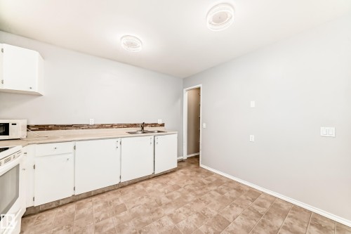 Kitchen featuring white cabinetry, light countertops, and white appliances - 5308 20 Avenue, Edmonton, AB - Indoor Photo Showing Kitchen With Double Sink