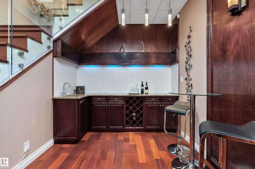 Indoor wet bar with dark wood finish cabinetry, light stone counters, dark wood-type flooring, and hanging light fixtures - 169 Callaghan Drive, Edmonton, AB - Indoor