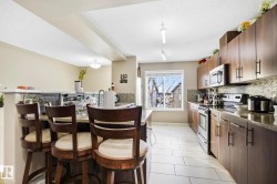 Kitchen featuring stainless steel appliances, dark stone counters, a textured ceiling, a kitchen breakfast bar, and dark brown cabinets - 
