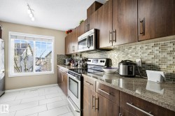 Kitchen with appliances with stainless steel finishes, dark stone counters, a textured ceiling, light tile patterned floors, and tasteful backsplash - 