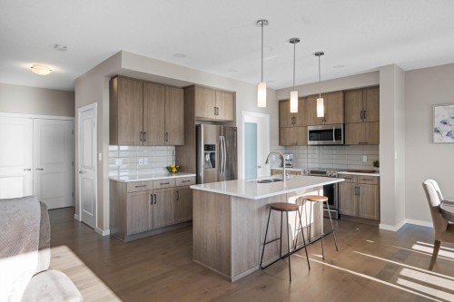 Kitchen with a breakfast bar area, stainless steel appliances, hanging light fixtures, wood finish cabinetry, and a kitchen island with sink - 3904 5 Street, Edmonton, AB - Indoor Photo Showing Kitchen With Stainless Steel Kitchen With Upgraded Kitchen