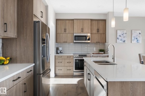 Kitchen with stainless steel appliances, light stone counters, hanging light fixtures, an island with sink, and decorative backsplash - 3904 5 Street, Edmonton, AB - Indoor Photo Showing Kitchen With Stainless Steel Kitchen With Double Sink With Upgraded Kitchen