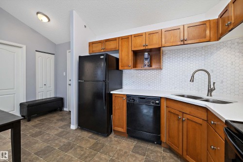 Kitchen featuring wood finish cabinetry, black appliances, light stone countertops, decorative backsplash, and stone finish floors - 2407 320 Clareview Station Drive, Edmonton, AB - Indoor Photo Showing Kitchen With Double Sink