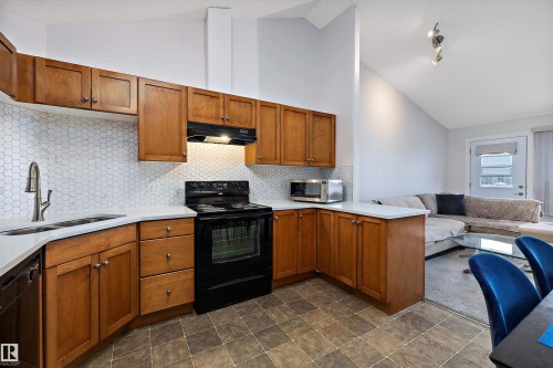 Kitchen featuring wood finish cabinets, black appliances, open floor plan, vaulted ceiling, and a peninsula - 2407 320 Clareview Station Drive, Edmonton, AB - Indoor Photo Showing Kitchen With Double Sink