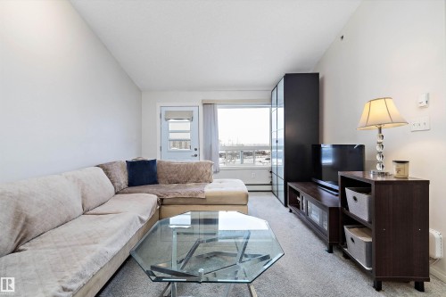 Living room featuring light carpet, lofted ceiling, and a baseboard heating unit - 2407 320 Clareview Station Drive, Edmonton, AB - Indoor Photo Showing Living Room