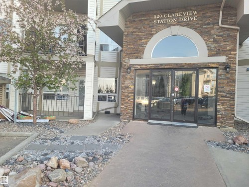 The property features an entrance with a stone facade, glass doors, and an arched window above - 2407 320 Clareview Station Drive, Edmonton, AB - Outdoor