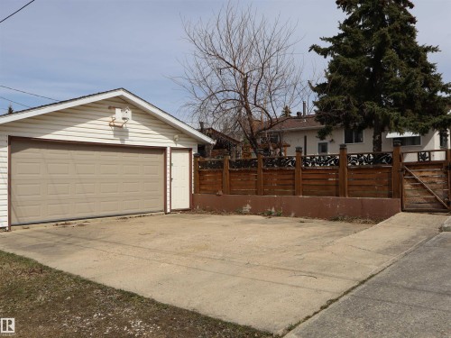 Detached garage with tan panel door, white siding, and an adjacent side entry door - 5220 - 56 Street, Barrhead, AB - Outdoor
