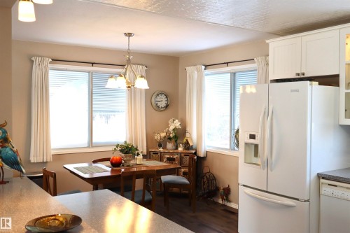 Kitchen featuring white dishwasher, dark wood-type flooring, hanging lights, white cabinets, and glass insert cabinets - 5220 - 56 Street, Barrhead, AB - Indoor