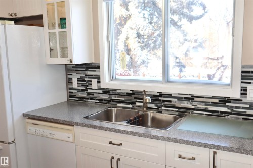 Kitchen with glass fronted cabinets, dark countertops, white cabinetry, dishwasher, and plenty of natural light - 5220 - 56 Street, Barrhead, AB - Indoor Photo Showing Kitchen With Double Sink