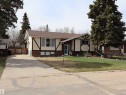 Split-level residence featuring a brown shingle roof, brick and stucco exterior, prominent dark trim detailing, a concrete driveway, and established front yard landscaping - 5220 - 56 Street, Barrhead, AB  - Outdoor With Facade 