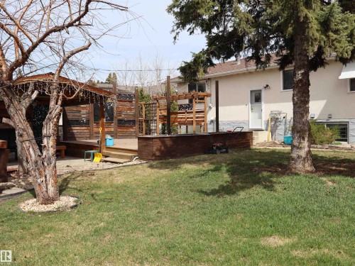Expansive backyard featuring a multi-level wood deck, a covered gazebo structure, and mature trees - 5220 - 56 Street, Barrhead, AB - Outdoor